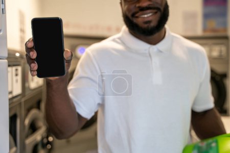 Photo for Cropped photo of a smiling bearded man holding a bottle of detergent and the smartphone in front of the camera - Royalty Free Image