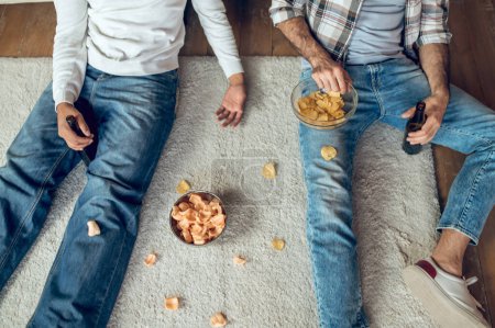 Photo for Cropped photo of men with bottles of beer and bowls of chips sitting on the mat - Royalty Free Image