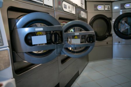 Photo for Interior of a public self-service laundromat with several commercial heavy-duty front-load washers arranged in a row - Royalty Free Image