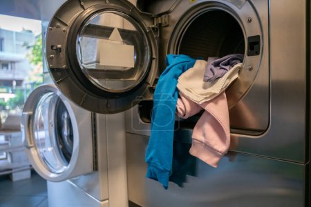 Lavadora automática abierta cargada con una pila de ropa sucia en una lavandería pública