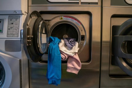 Open clothes washer loaded with a pile of dirty laundry at a communal self-service laundromat