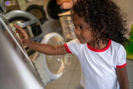 Photo for Focused cute child standing before a washing machine and pressing buttons on the control panel - Royalty Free Image