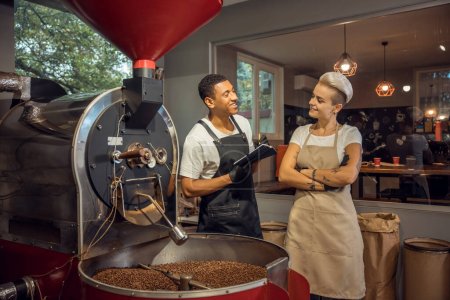 Foto de Alegre joven maestro asado hablando con su colega mujer contenta en una instalación de tostado de café - Imagen libre de derechos