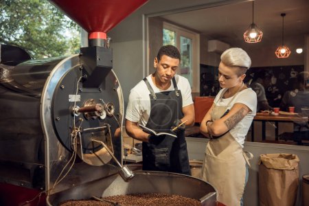 Photo for Serious focused young professional roast master perusing the coffee roasting journal in her colleague hands - Royalty Free Image