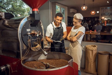 Photo for Smiling pleased professional roaster showing notes in the coffee roasting journal to his female colleague - Royalty Free Image