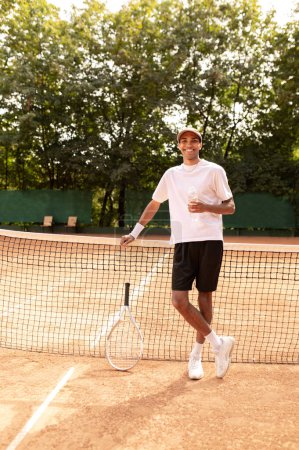 Foto de Jugador de tenis. Joven en thsirt blanco de pie en la cancha de tenis - Imagen libre de derechos