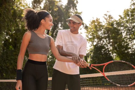 Foto de Entrenamiento. Joven entrenador masculino enseñando a una chica de pelo rizado a jugar al tenis - Imagen libre de derechos