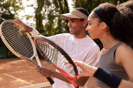 Foto de Entrenamiento. Joven entrenador masculino enseñando a una chica de pelo rizado a jugar al tenis - Imagen libre de derechos
