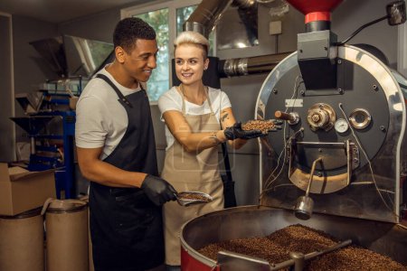 Photo for Cheerful young worker and his smiling female colleague determining the roast degree of coffee beans - Royalty Free Image