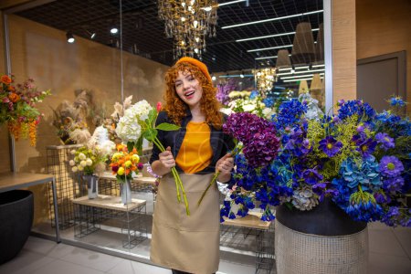 Téléchargez les photos : Dans un magasin de fleurs. Mignon fille souriante avec des fleurs regardant apprécié - en image libre de droit