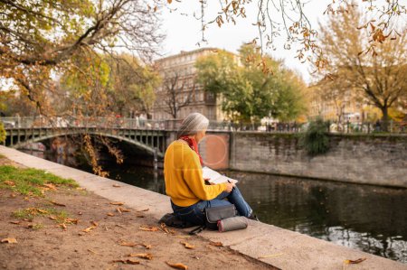 Foto de Humor creativo. Mujer sentada en la orilla del río y tomando notas - Imagen libre de derechos