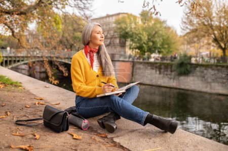 Photo for Inspiration. Woman sitting on the river bank, making notes and looking inspired - Royalty Free Image