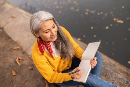 Photo for Artist. Mature woman sitting on the river bank and drawing in album - Royalty Free Image