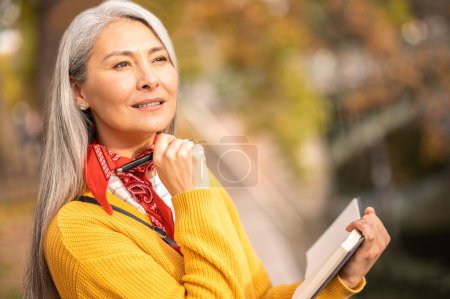 Téléchargez les photos : Inspiration d'automne. Belle femme mûre avec un cahier dans les mains à la recherche inspiré - en image libre de droit