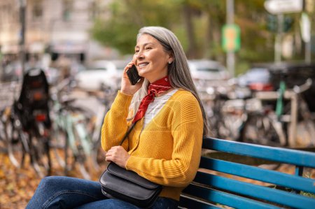 Foto de Llamada telefónica. Mujer guapa sentada en el banco y hablando por teléfono - Imagen libre de derechos