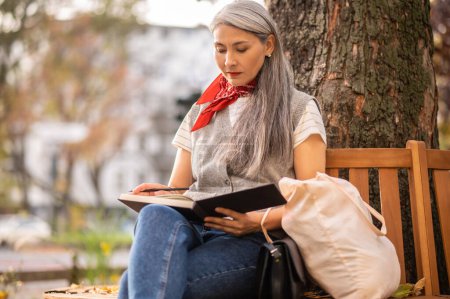 Foto de Inspiración. Mujer sentada en un banco con un cuaderno y mirando involucrada - Imagen libre de derechos