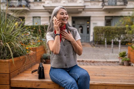 Foto de Llamada telefónica. Mujer de pelo largo sentada en el banco y hablando por teléfono - Imagen libre de derechos