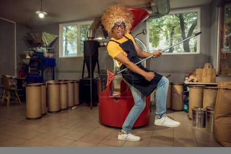Photo for Full-size portrait of a joyful funny cleaner in the wig playing the broom guitar during the cleaning - Royalty Free Image