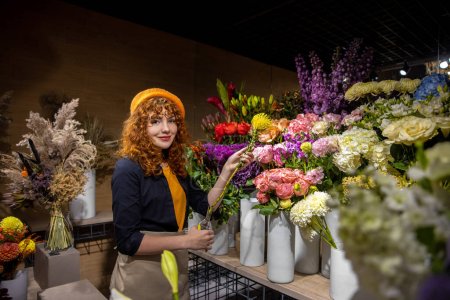 Téléchargez les photos : Fleuriste au travail. Jolie fleuriste triant les fleurs et regardant impliqué - en image libre de droit