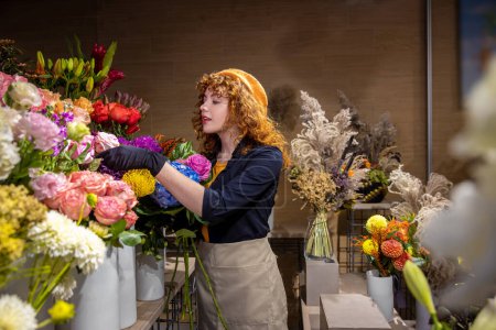 Téléchargez les photos : Dans un magasin de fleurs. Fleuriste aux cheveux bouclés souriant avec des fleurs - en image libre de droit