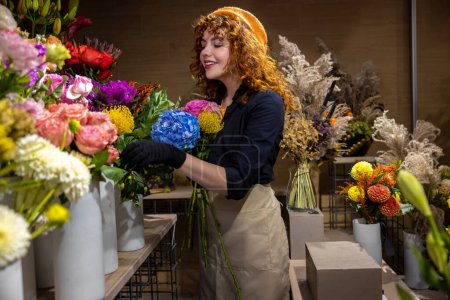 Lovely florist. Ginger young woman in a flower shop looking romantic and contented
