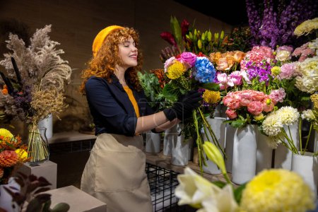 Téléchargez les photos : Beau fleuriste. Gingembre jeune femme dans un magasin de fleurs à la recherche romantique et satisfait - en image libre de droit