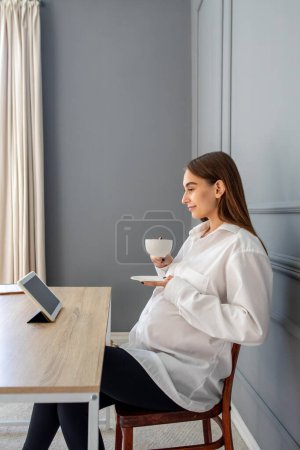Foto de Embarazada en el trabajo. Embarazada joven mujer de negocios en su oficina por la mañana - Imagen libre de derechos