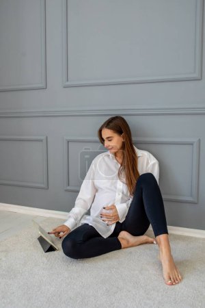 Photo for Feeling comfortable. Long-haired cute pregnant woman sitting on the floor with a laptop - Royalty Free Image
