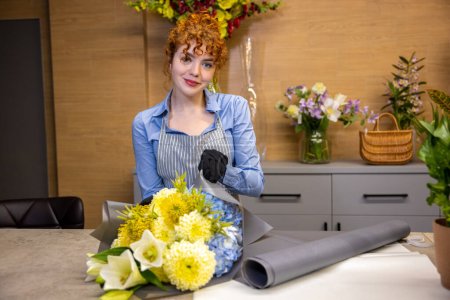 Téléchargez les photos : Dans un magasin de fleurs. Mignon roux jeune femme debout à la table dans un magasin de fleurs - en image libre de droit
