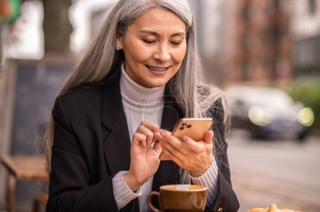 Photo for Chatting. Long-haired mature woman texting on the phone and looking involved - Royalty Free Image