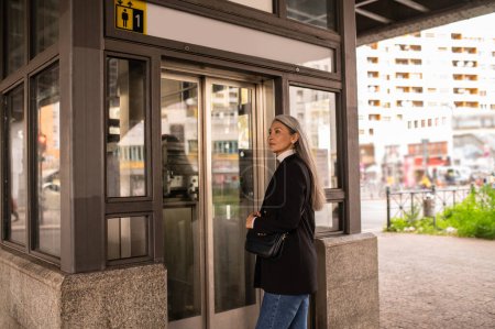 Foto de En la entrada. Mujer de pelo largo con un abrigo negro que entra en el metro - Imagen libre de derechos