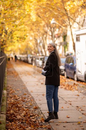Foto de Mujer en el parque de otoño. Mujer madura de pelo largo y bien parecido en la calle del parque de otoño - Imagen libre de derechos