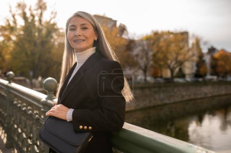 Photo for Bridge. Cute mid aged woman in a black coat standing on the river river bridge - Royalty Free Image