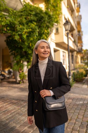 Foto de Mujer sonriente. Mujer sonriente con un abrigo negro en la calle de la ciudad - Imagen libre de derechos