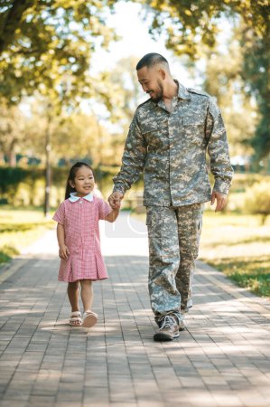 Foto de Fin de semana juntos. Militar caminando con su pequeña hija en el parque - Imagen libre de derechos