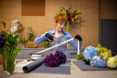 Photo for Florist at work. Cute ginger florist looking involved while making a cover for the bouquet - Royalty Free Image