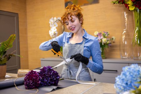 Foto de Florista en el trabajo. Linda florista de jengibre mirando involucrado mientras que hace una cubierta para el ramo - Imagen libre de derechos