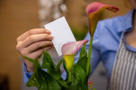 Photo for Card in a bouquet. Close up of female hand putting a card in a bouquet - Royalty Free Image