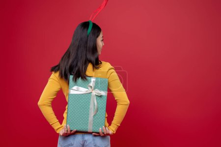 Foto de Esconder un regalo. Mujer joven en sombrero de ciervo con ocultar una caja de regalo - Imagen libre de derechos