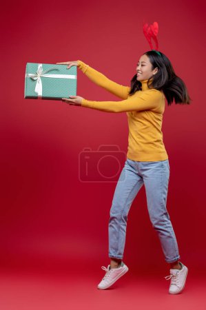 Photo for Xmas rush. Dark-haired young woman in deer hat with a surprise box in hands jumping - Royalty Free Image