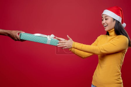 Téléchargez les photos : Cadeau de Noël. Jeune femme excitée en chapeau de Père Noël recevant un cadeau de Noël - en image libre de droit