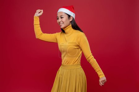 Téléchargez les photos : Noël. Jolie femme asiatique mince en robe jaune et chapeau de Père Noël - en image libre de droit