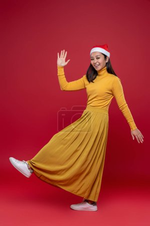 Foto de En Navidad. Bastante delgado asiático mujer en amarillo vestido y santa hat - Imagen libre de derechos