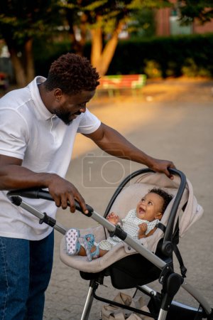 Téléchargez les photos : En promenade avec un gosse. Jeune homme afro-américain avec son enfant dans le parc - en image libre de droit