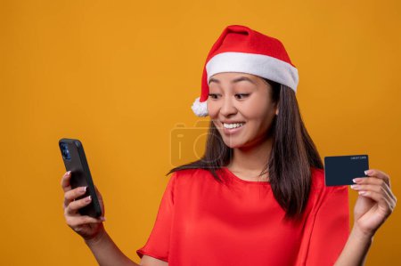 Photo for Payment by card. Young woman in red making orders on the phone and paying by card - Royalty Free Image