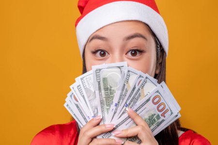 Téléchargez les photos : Les courses de Noël. Jeune femme en santa chapeau avec des dollars dans les mains - en image libre de droit