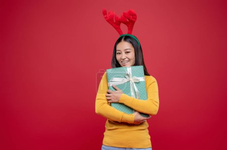 Téléchargez les photos : Cadeau de Noël. Jeune femme brune en chapeau de cerf avec une boîte surprise dans les mains - en image libre de droit