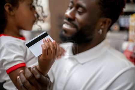 Cute family on shopping. African american man holding his kid, the girl holding a credit card and smiling