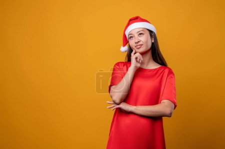 Téléchargez les photos : Dans les pensées. Jeune femme en robe rouge et chapeau de Père Noël penser à des idées de surprises - en image libre de droit