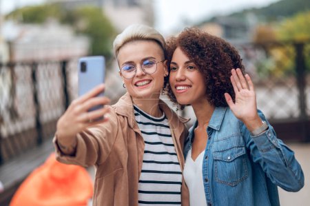 Foto de Retrato en la cintura de una mujer alegre fotografiándose a sí misma y a su amiga feliz con la cámara del smartphone - Imagen libre de derechos